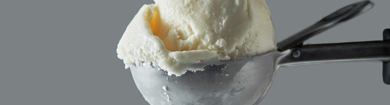Close-up delicious dairy dessert cold white vanilla in a metal spoon for ice cream on a gray background. Summer concept. Space for text.